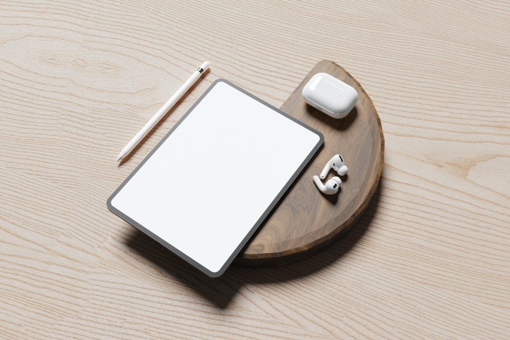 a wooden table with a tablet, pen, and earbuds on it